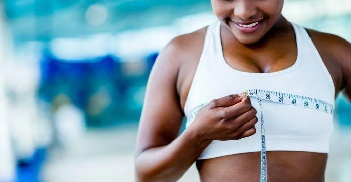 Fit woman measuring her top wearing a sports bra