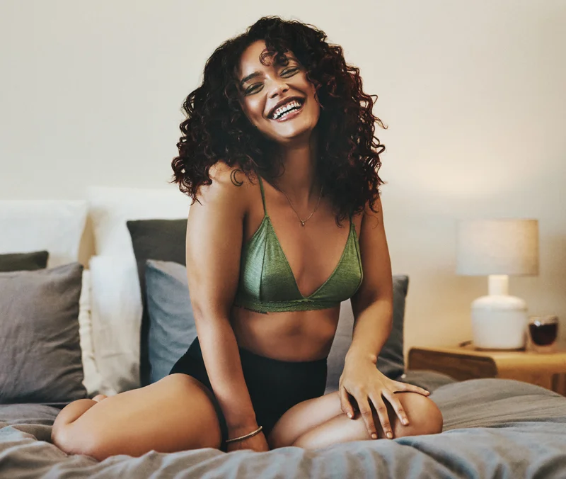 Curly-haired woman in green top on her bed