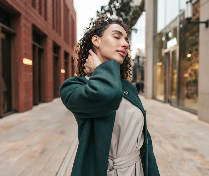 Woman outside between buildings posing with her hand to her neck